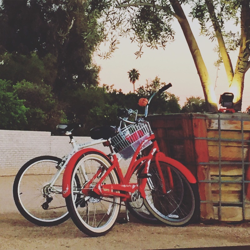 A pair of bikes, red and white parked on a sidewalk. 